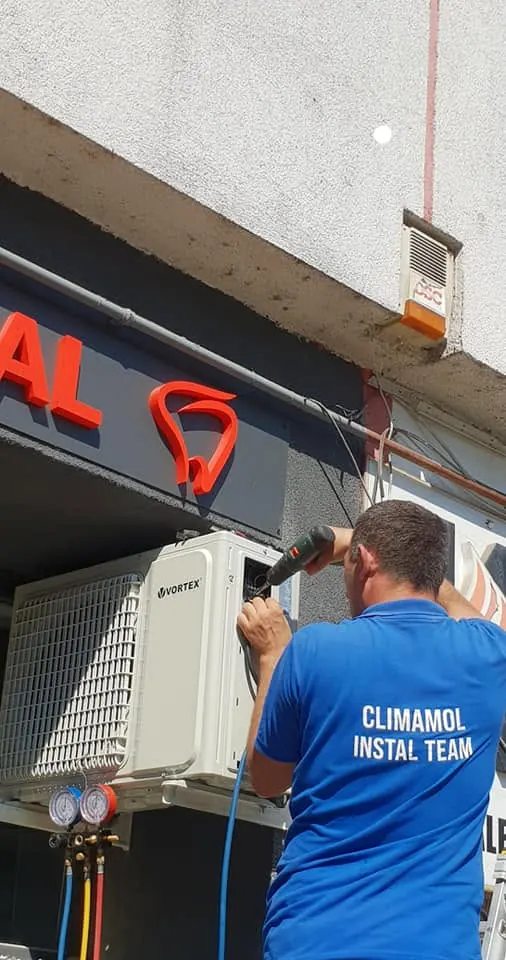 Coleg Climamol cu tricoul echipei, vidând instalația unui aparat de aer condiționat cu manometrele